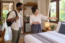 A hotel owner shows a traveler a clean guest room before they decide how to book.