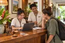 A front-desk clerk records a direct booking inquiry on a laptop while a guest waits.